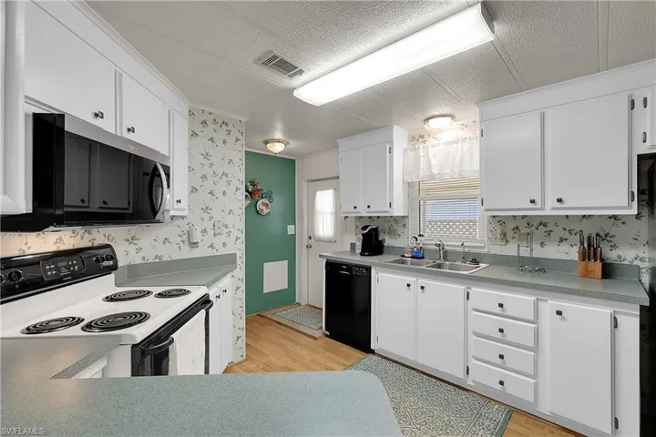 Kitchen with electric stove, a textured ceiling, stainless steel microwave, white cabinetry, and wallpapered walls