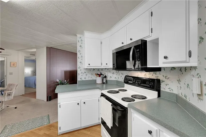 Kitchen featuring electric range oven, white cabinetry, light wood finished floors, a textured ceiling, and stainless steel microwave