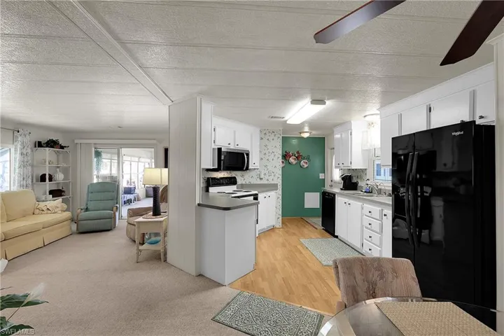 Kitchen featuring open floor plan, black appliances, white cabinets, a textured ceiling, and light countertops