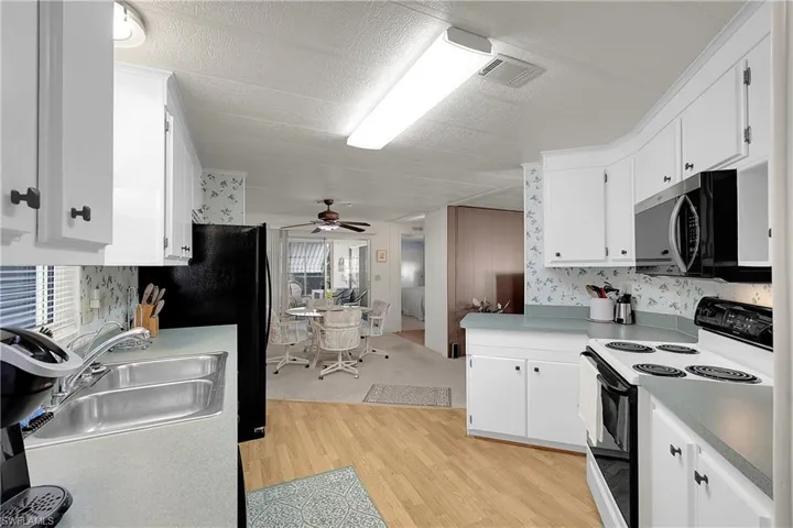 Kitchen with electric stove, white cabinetry, freestanding refrigerator, light wood finished floors, and a textured ceiling