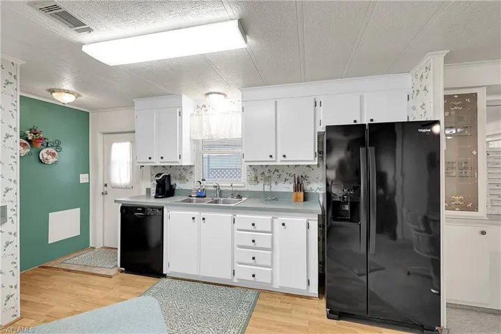 Kitchen featuring black appliances, a textured ceiling, white cabinets, light wood-style floors, and light countertops