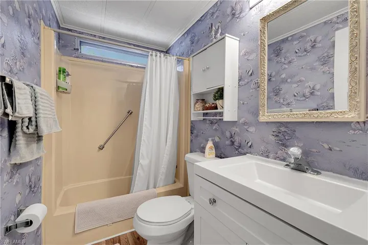 Full bath featuring wallpapered walls, vanity, shower / bathtub combination with curtain, and crown molding