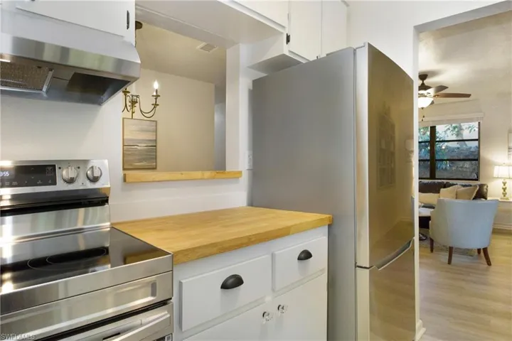 Kitchen with wall chimney range hood, light luxury vinyl wood-style floors, white cabinets, stainless steel range with electric stove top, and stainless fridge