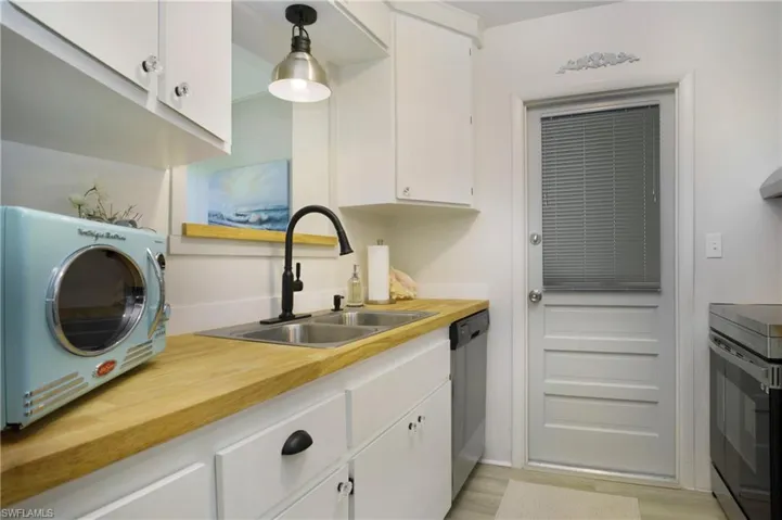 Kitchen featuring dishwasher, hanging light fixtures, butcher block countertops, white cabinets, and sink