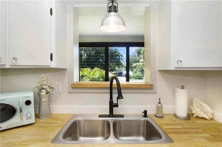 Kitchen with hanging light fixtures, white cabinets, sink, retro microwave and luxury vinyl wood-style flooring