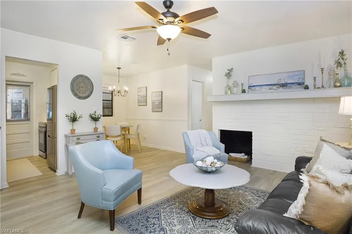 Living room with a faux brick fireplace, luxury vinyl wood-style flooring, and ceiling fan with notable chandelier