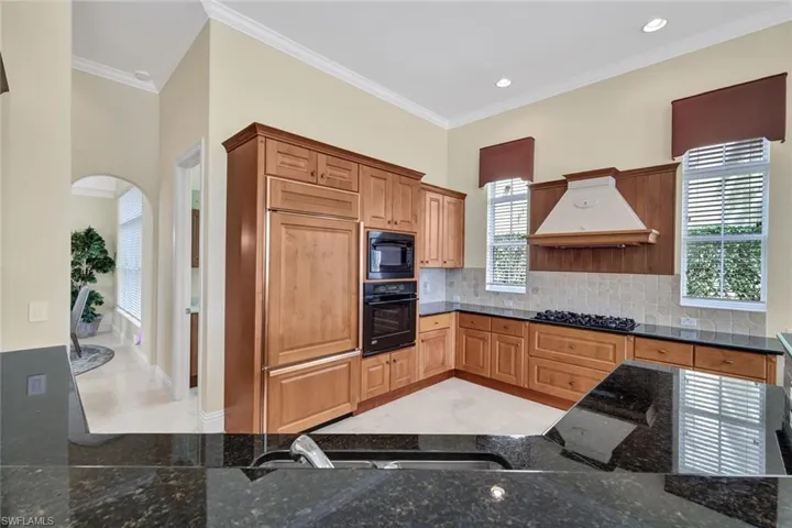 Kitchen with dark stone countertops, crown molding, light tile patterned floors, black appliances, and premium range hood