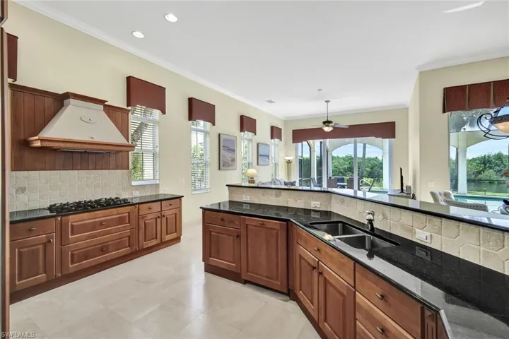 Kitchen with dark stone countertops, gas cooktop, custom range hood, and backsplash