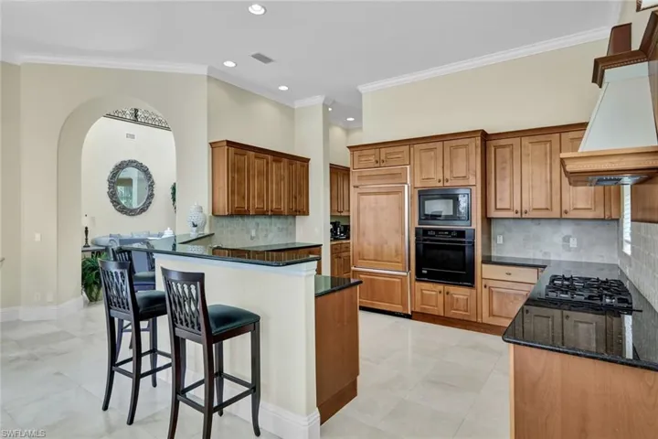 Kitchen featuring dark stone countertops, black appliances, kitchen peninsula, decorative backsplash, and ornamental molding