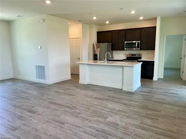 Kitchen with dark brown cabinets, stainless steel appliances, a kitchen island with sink, open floor plan, and recessed lighting