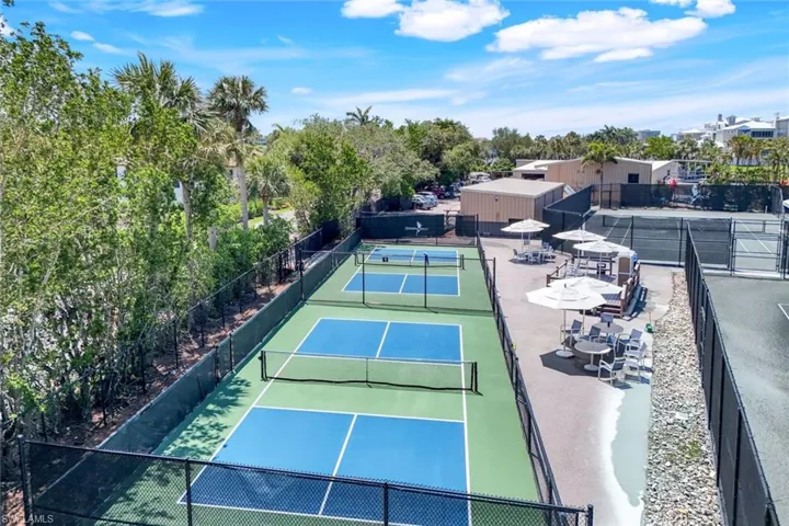 View of tennis court featuring fence and view of scattered trees