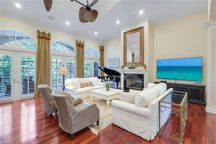 Living area featuring arched walkways, ornate columns, ceiling fan, dark wood-style floors, and a fireplace