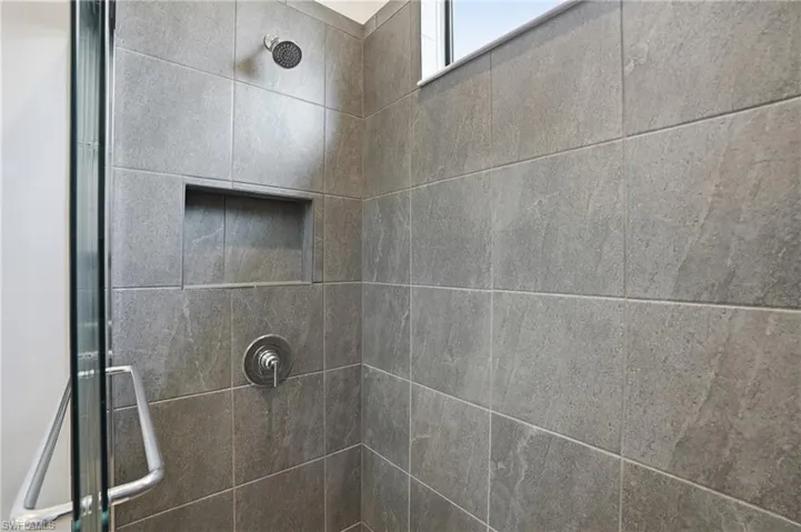 Shower featuring large-format grey wall tiles, a built-in shower niche, and a glass enclosure with a polished chrome handle