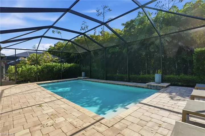 Screened enclosure featuring a rectangular swimming pool with integrated steps, surrounded by light-colored paver decking