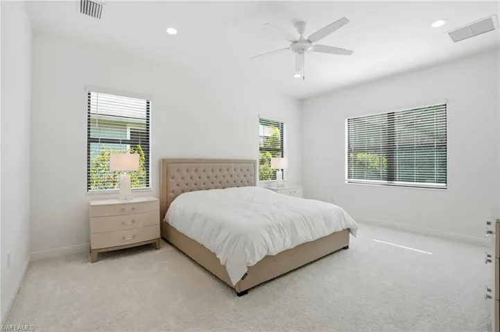 Spacious room featuring light-toned carpeting, white walls, and multiple windows with horizontal blinds