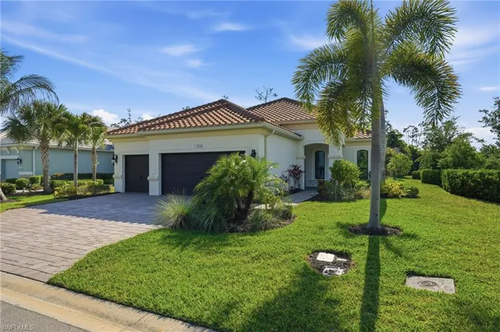Mediterranean-style residence featuring a tile roof, stucco exterior, two-car garage with dark doors, and a paver driveway