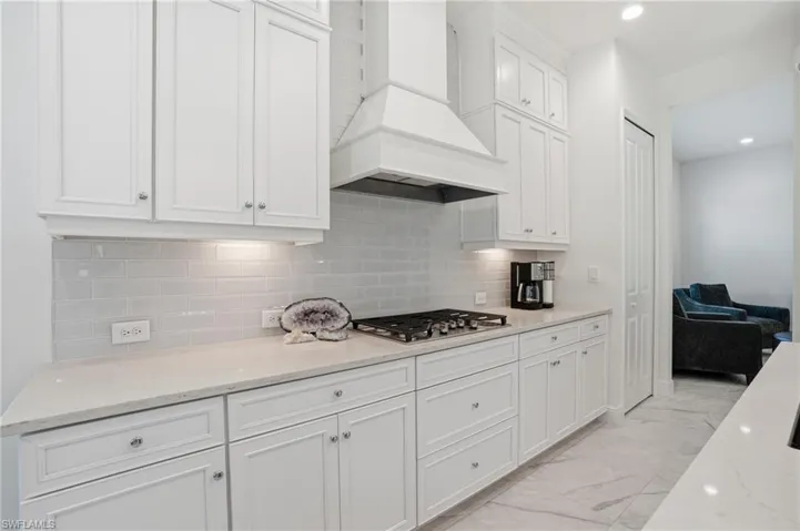 Bright kitchen featuring white shaker cabinetry, light-toned countertops, a subway tile backsplash, a gas cooktop, and recessed lighting