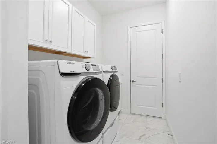 Laundry area featuring shaker-style upper cabinetry with crystal knobs, wood-finish shelving, and white tile flooring