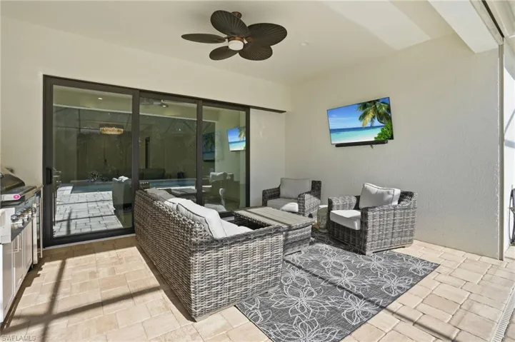 Expansive covered lanai featuring a ceiling fan, tiled flooring, and a built-in outdoor kitchen with grill