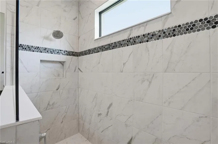 Shower enclosure featuring large format white tiled walls with subtle gray veining, accented by a horizontal band of hexagonal mosaic tiles