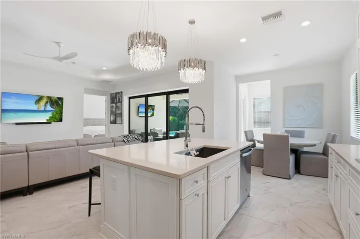 Open-concept kitchen and living area featuring a central island with an undermount sink, pendant lighting, white cabinetry, and light-toned flooring