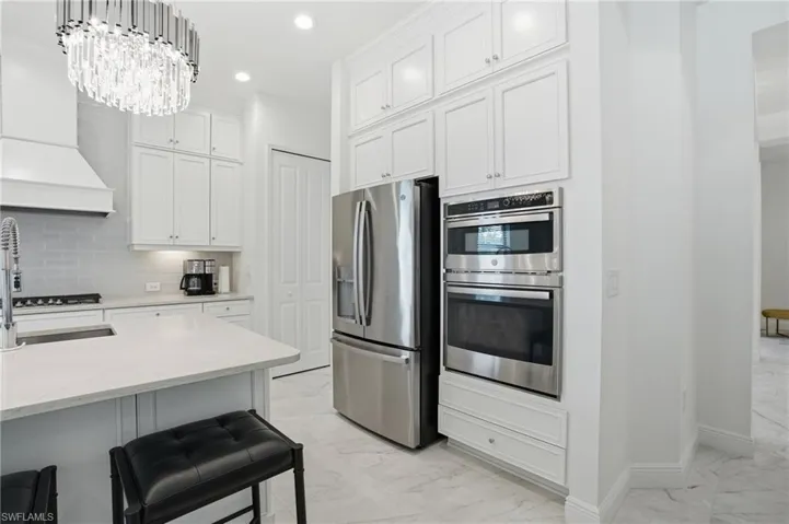 Gourmet kitchen with white shaker cabinetry, stainless steel appliances, a built-in oven and microwave, and a large central island with a sink