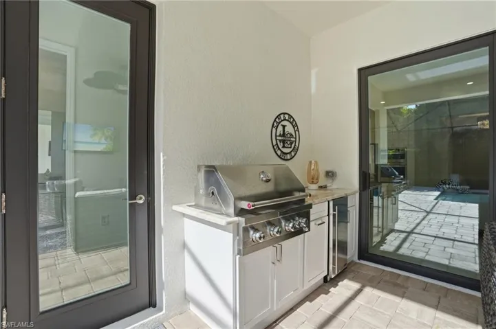 Outdoor kitchen with a built-in stainless steel grill, under-counter refrigerator, white cabinetry, and a light-toned countertop