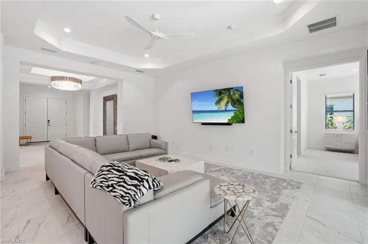 Spacious living area featuring large format tile flooring, crown molding, a tray ceiling with recessed lighting, and a modern ceiling fan