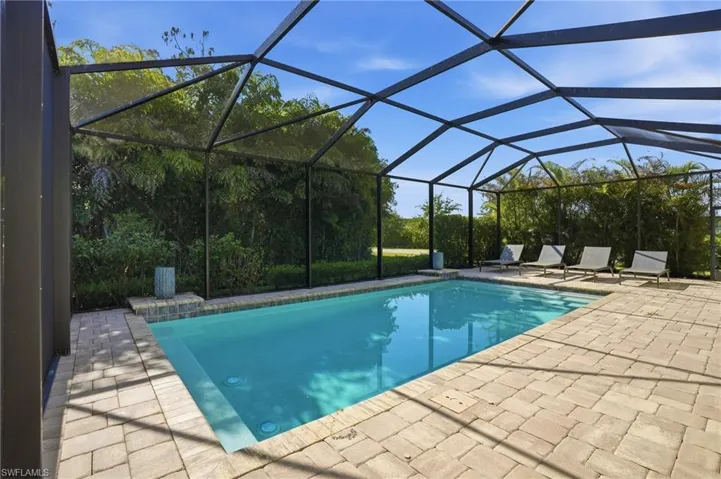 Screened outdoor pool area featuring a rectangular pool with light blue tiling, surrounded by light-toned paver decking