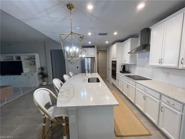 Kitchen featuring a breakfast bar area, a center island with sink, white cabinets, light stone counters, and hanging light fixtures