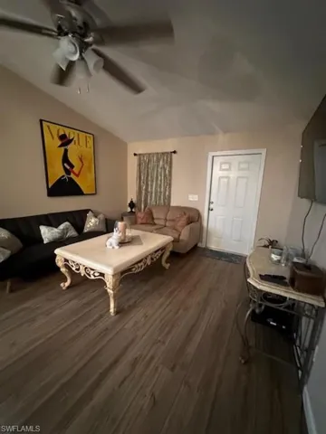 Living room with ceiling fan, vaulted ceiling, and dark wood-type flooring