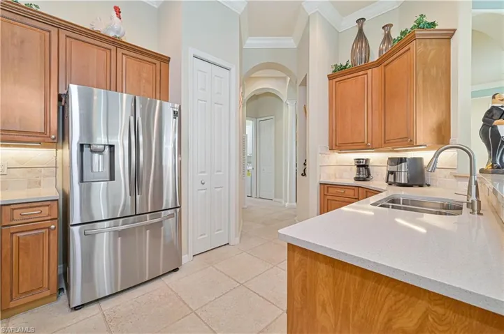 Kitchen featuring arched walkways, light stone countertops, stainless steel fridge with ice dispenser, tasteful backsplash, and wood finish cabinetry
