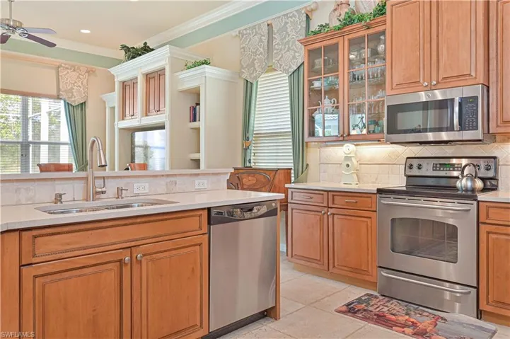 Kitchen featuring stainless steel appliances, wood finish cabinets, decorative backsplash, ornamental molding, and light stone counters