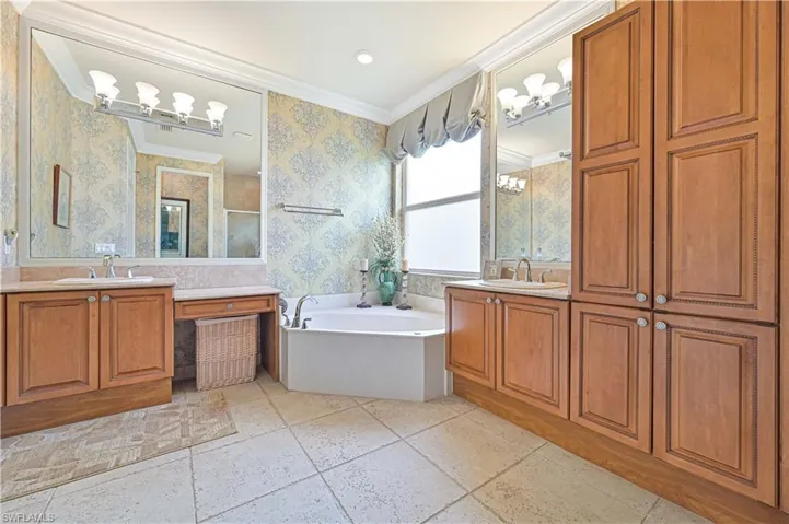 Bathroom featuring ornamental molding, two vanities, a bath, and a stall shower
