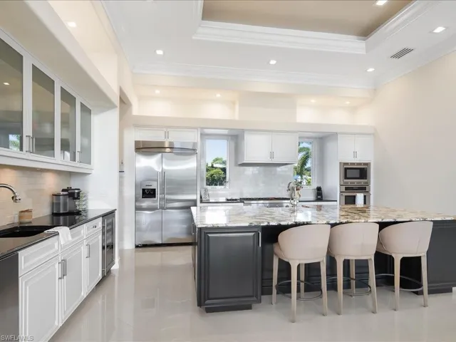Two tone kitchen featuring built in appliances, dark stone counters, glass insert cabinets, backsplash, and two tone color scheme