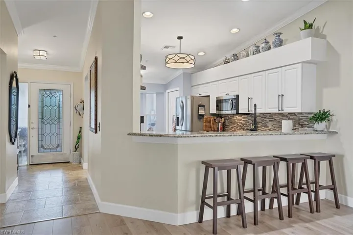 Kitchen featuring stainless steel appliances, baseboards, decorative backsplash, light stone countertops, and a breakfast bar