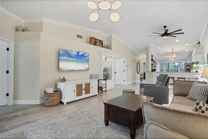 Living area featuring crown molding, light wood-style flooring, ceiling fan, baseboards, and lofted ceiling