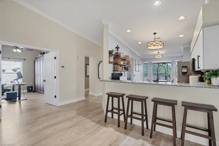 Kitchen with freestanding refrigerator, ornamental molding, light wood-style floors, a breakfast bar area, and white cabinets