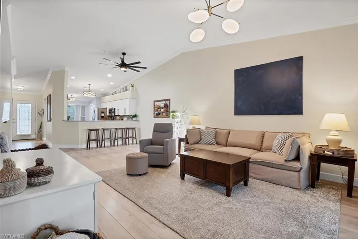 Living room featuring crown molding, light wood-style floors, ceiling fan, vaulted ceiling, and baseboards