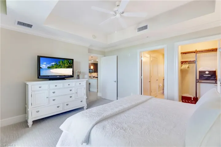 Carpeted bedroom with a raised ceiling, a ceiling fan, crown molding, and a walk in closet