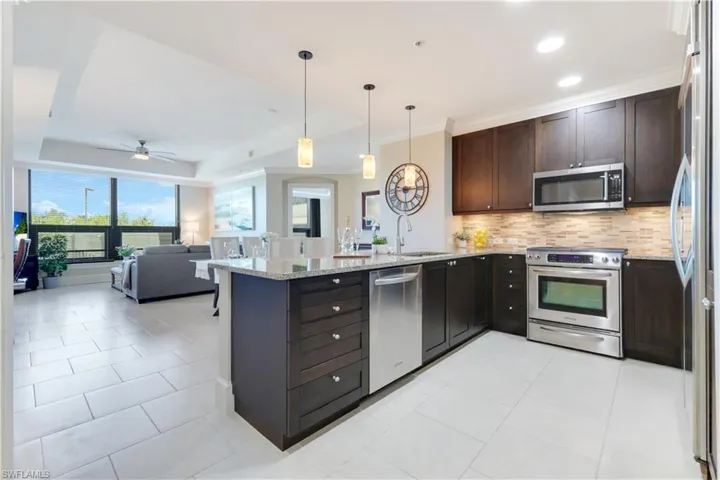 Kitchen featuring a raised ceiling, appliances with stainless steel finishes, dark brown cabinetry, tasteful backsplash, and hanging light fixtures