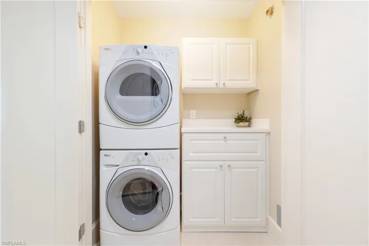 Washroom with cabinet space, stacked washer / drying machine, and light tile patterned floors