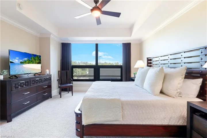 Bedroom featuring light colored carpet, a raised ceiling, a ceiling fan, and ornamental molding