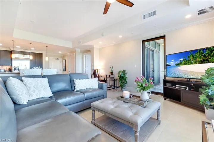 Living room featuring a tray ceiling, recessed lighting, a ceiling fan, crown molding, and light tile patterned floors
