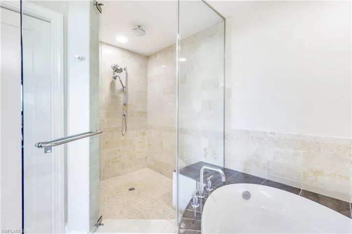 Bathroom featuring a garden tub, a shower stall, and tile walls