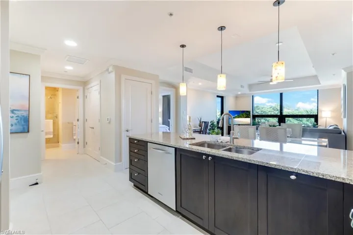 Kitchen with crown molding, hanging light fixtures, open floor plan, stainless steel dishwasher, and a tray ceiling
