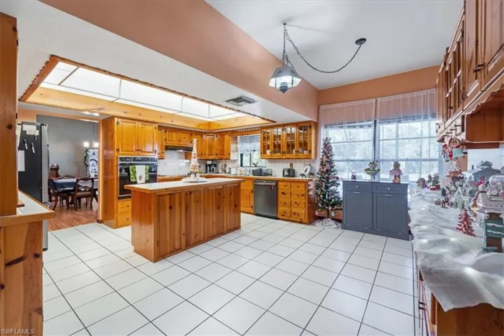 Kitchen featuring a kitchen island, backsplash, decorative light fixtures, light tile patterned floors, and appliances with stainless steel finishes