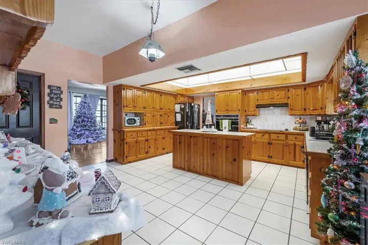 Kitchen featuring a kitchen island, backsplash, decorative light fixtures, light tile patterned floors, and black appliances