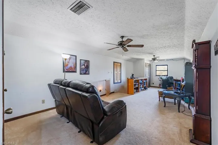 Living room with vaulted ceiling, light carpet, ceiling fan, and a textured ceiling