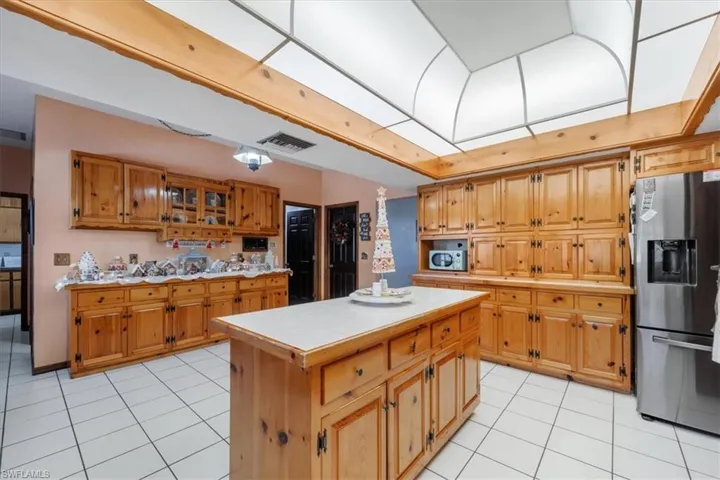 Kitchen featuring tile counters, a kitchen island, light tile patterned floors, and appliances with stainless steel finishes